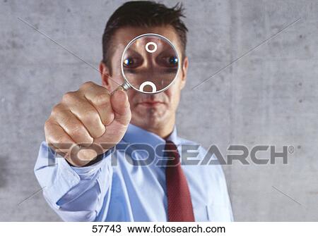 Stock Image - Close-up of man holding magnifying glass in front of his face . Fotosearch