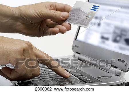 Stock Image - Close-up of person's hands holding credit card and using laptop . Fotosearch