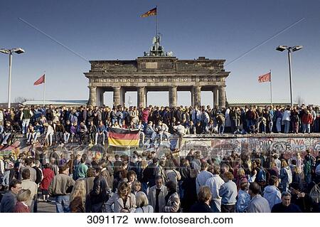 Fall of the Berlin Wall: people from East and West Berlin climbing on the Wall at the Brandenburg Gate, Berlin, Germany View Large Photo Image Stock Image - Fall of the Berlin Wall: people from East and West Berlin climbing on the Wall at the Brandenburg Gate, Berlin, Germany . Fotosearch
