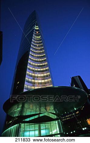 Stock Image - Low angle view of office building lit up at dusk, La Defense, Paris, Ile-De-France, France . Fotosearch