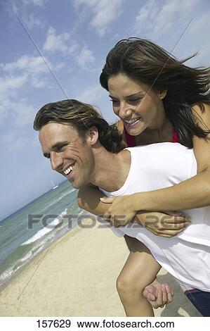 Mid adult man giving piggyback to young woman on beach View Large Photo Image Stock Photo - Mid adult man giving piggyback to young woman on beach . Fotosearch