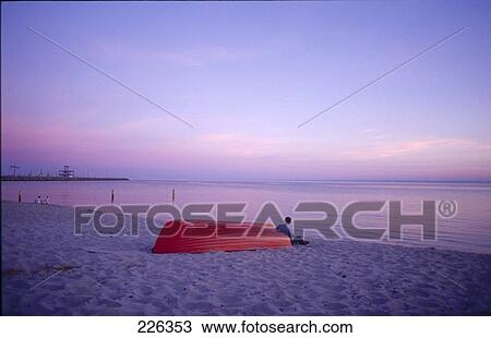 Person sitting leaning against boat on beach, Poland View Large Photo Image Stock Image - Person sitting leaning against boat on beach, Poland . Fotosearch