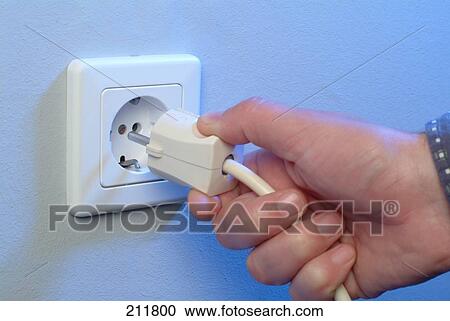 Stock Image - Person's hand inserting plug into socket . Fotosearch