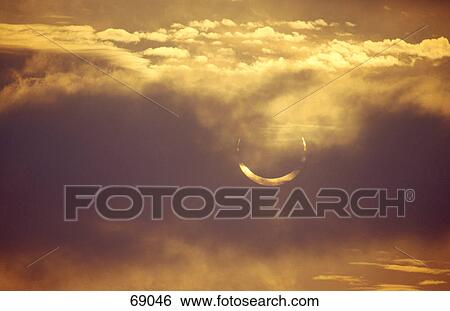 Solar eclipse behind clouds in sky View Large Photo Image Stock Photograph - Solar eclipse behind clouds in sky . Fotosearch