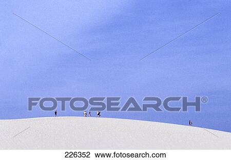 Stock Image - Tourists standing on sand dune against sky, Slowinski National Park, Poland . Fotosearch