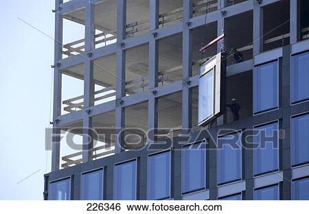 Window handing from crane in front of building under construction View Large Photo Image Stock Photograph - Window handing from crane in front of building under construction . Fotosearch