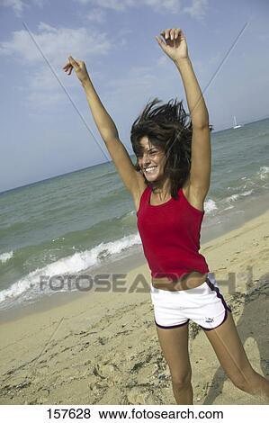 Young woman smiling and raising her arms on beach View Large Photo Image Stock Photo - Young woman smiling and raising her arms on beach . Fotosearch