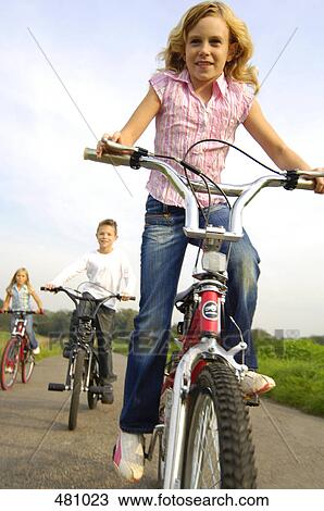 Stock Image - Bother and sisters cycling through field . Fotosearch