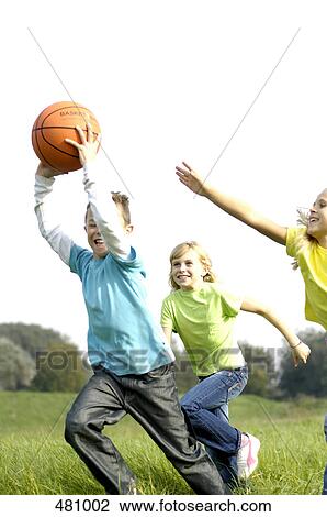 Stock Image - Brother and sisters playing basketball in field . Fotosearch