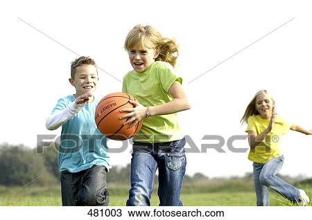 Stock Image - Brother and sisters playing basketball in field . Fotosearch