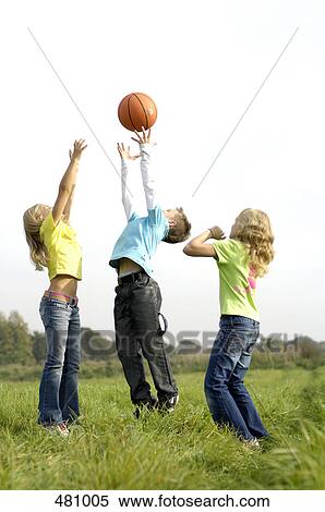 Stock Photography - Brother and sisters playing basketball in field . Fotosearch