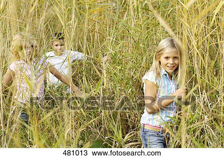 Stock Image - Brother and sisters playing in field . Fotosearch