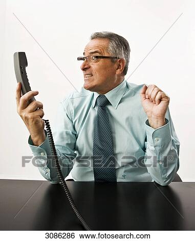 Businessman looking angry at a phone receiver in his hand View Large Photo Image Stock Photograph - Businessman looking angry at a phone receiver in his hand . Fotosearch