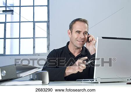 Businessman talking on mobile phone in office View Large Photo Image Stock Image - Businessman talking on mobile phone in office . Fotosearch