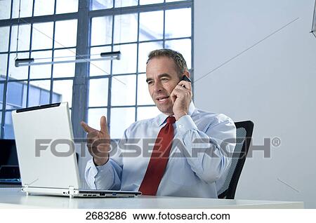 Stock Photograph - Businessman talking on mobile phone in office . Fotosearch