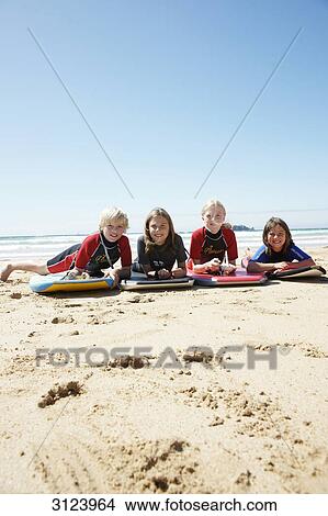 Picture - Children lying with surfboards on the beach, front view . Fotosearch
