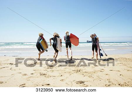 Stock Image - Children with surfboards running into the water, rear view . Fotosearch