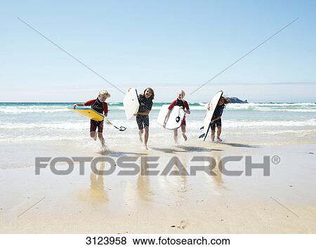 Stock Photo - Children with surfboards running out of the water, front view . Fotosearch