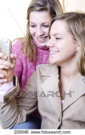 Stock Photograph - Close-up of teenage girls looking at mobile phone and smiling . Fotosearch