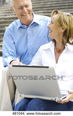 Picture - Close-up of woman holding laptop and looking at her husband . Fotosearch