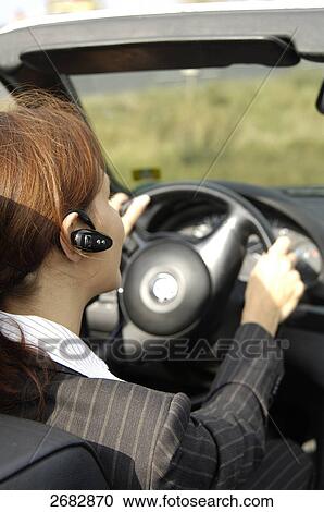 Stock Image - Close-up of woman using bluetooth while driving car . Fotosearch