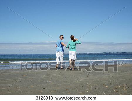 Stock Photo - Couple running into the water, rear view . Fotosearch