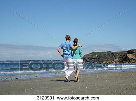 Stock Image - Couple walking along the beach, rear view . Fotosearch