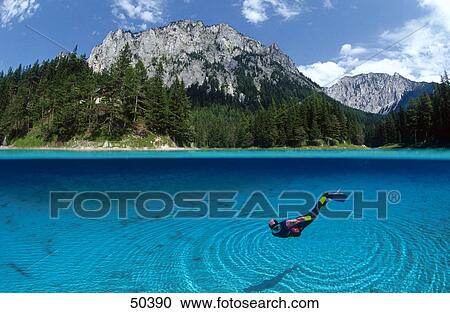 Stock Image - Diver diving in lake with mountain in background, Alpine Lake, Austria . Fotosearch