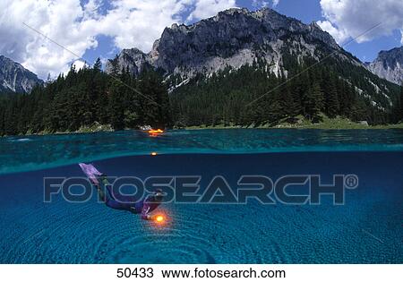 Stock Image - Diver diving in lake with mountain in background, Alpine Lake, Austria . Fotosearch