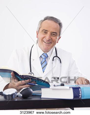 Doctor sitting at a desk, holding a book, portrait View Large Photo Image Stock Photo - Doctor sitting at a desk, holding a book, portrait . Fotosearch