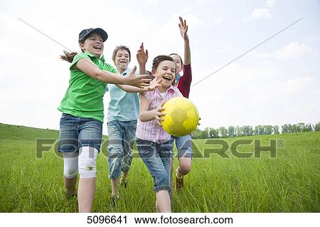 Stock Image - Four children playing with football in meadow . Fotosearch
