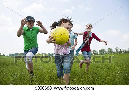 Stock Photo - Four children playing with football in meadow . Fotosearch