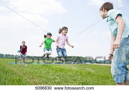 Stock Image - Four children skipping rope in meadow . Fotosearch