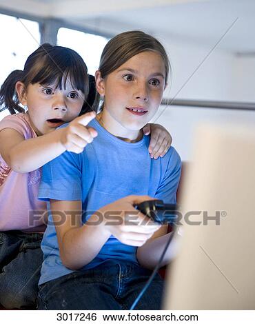 Girl playing a computer game while her sister is pointing at the screen View Large Photo Image Stock Photograph - Girl playing a computer game while her sister is pointing at the screen . Fotosearch