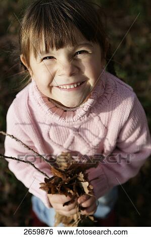 Stock Photograph - Girl with leaves looking at camera, elevated view . Fotosearch