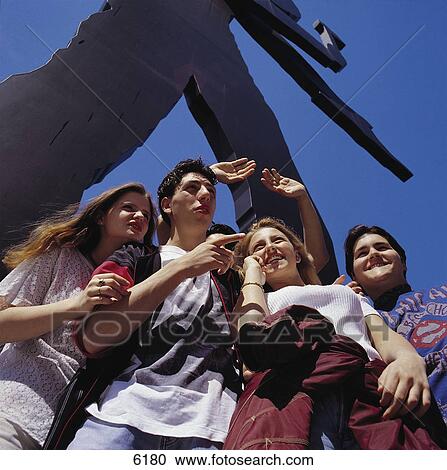 Stock Image - Group of teenagers standing in front of sculpture of hammering man, Frankfurt, Germany . Fotosearch