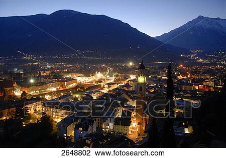 Stock Image - High angle view of city lit up at dusk, Meran, Trentino-Alto Adige, Italy . Fotosearch