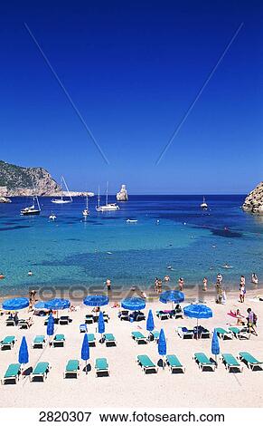 Stock Photo - High angle view of lounge chairs and tourists on beach, Cala Benirras, Ibiza, Balearic Islands, Spain . Fotosearch