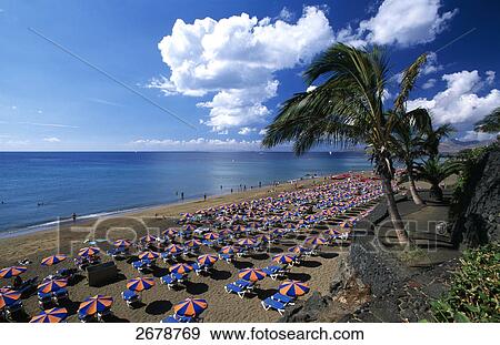 Stock Photo - High angle view of tourists and sunshades on beach, Playa Blanca, Puerto Del Carmen, Lanzarote, Canary Islands, Spain . Fotosearch