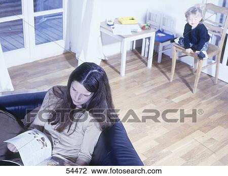 High angle view of woman reading book on sofa with her child sitting on chair in background View Large Photo Image Stock Image - High angle view of woman reading book on sofa with her child sitting on chair in background . Fotosearch
