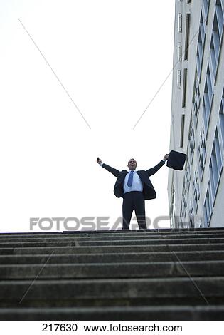 Stock Image - Low angle view of businessman stretching his arms in front of office building . Fotosearch