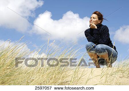 Low angle view of young woman crouching on beach View Large Photo Image Stock Photo - Low angle view of young woman crouching on beach . Fotosearch