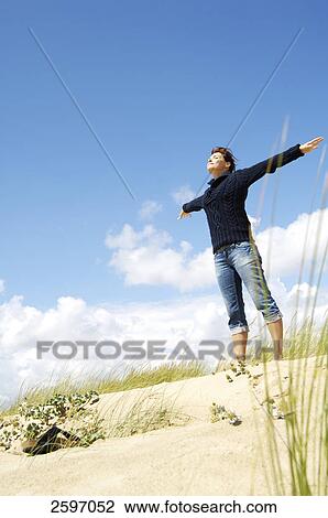 Stock Image - Low angle view of young woman stretching her arms on beach . Fotosearch