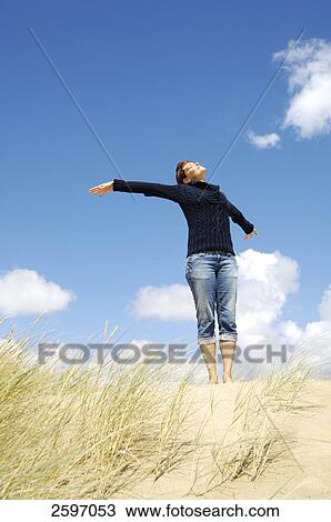 Stock Image - Low angle view of young woman stretching her arms on beach . Fotosearch