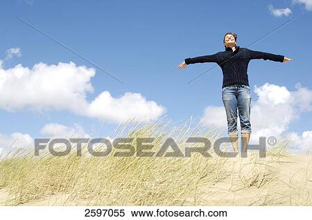 Stock Photography - Low angle view of young woman stretching her arms on beach . Fotosearch