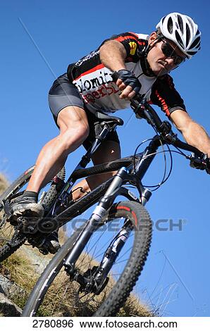 Stock Photograph - Male mountainbiker riding downhill, low angle view . Fotosearch