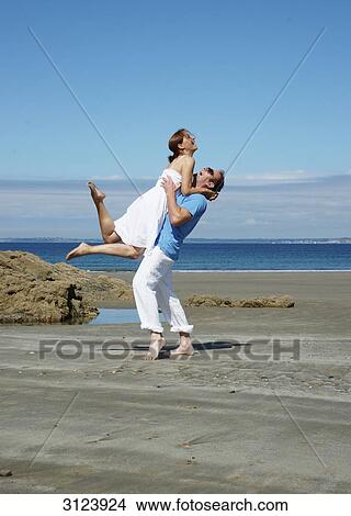 Man lifting woman on the beach, side view View Large Photo Image Picture - Man lifting woman on the beach, side view . Fotosearch