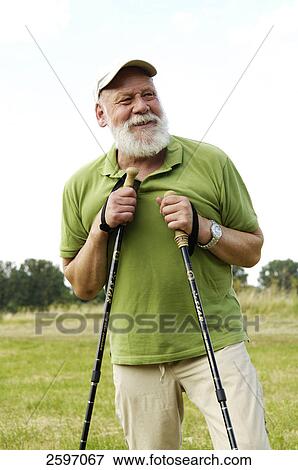 Mature man holding hiking poles and smiling in field View Large Photo Image Stock Photo - Mature man holding hiking poles and smiling in field . Fotosearch