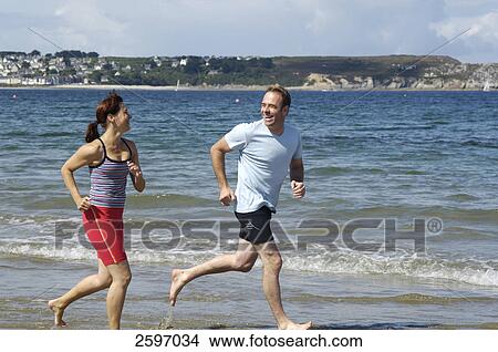 Picture - Mid adult couple jogging on beach . Fotosearch