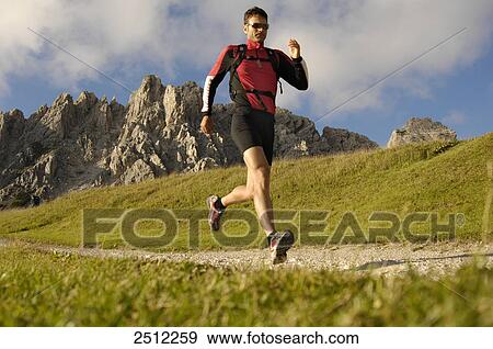 Stock Photo - Mid adult man running in field, Trentino-Alto Adige, Italy . Fotosearch